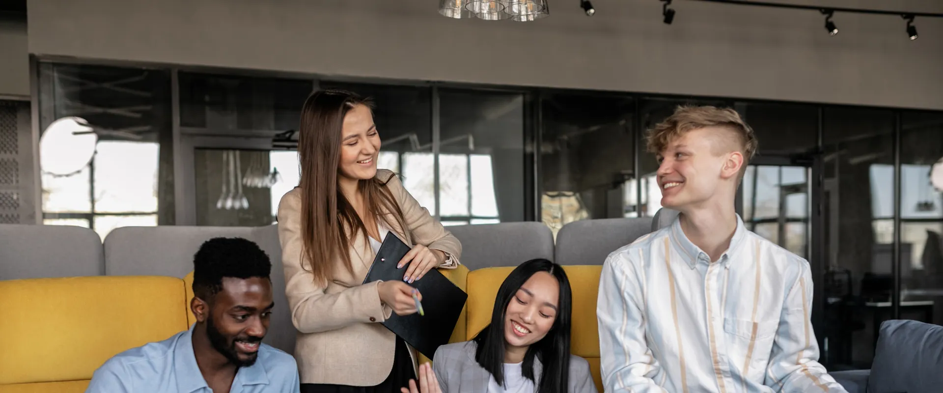 Groupe de jeunes professionnels souriants qui échangent sur un canapé dans un espace de travail moderne
