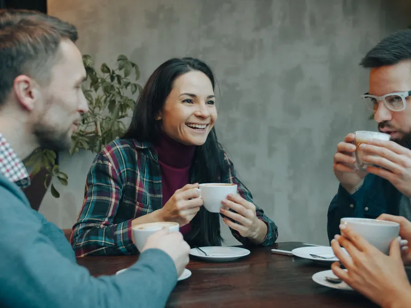 Groupe d'amis souriants qui échangent autour d'une table avec des cafés