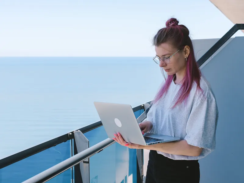 Femme travaillant sur son ordinateur portable depuis un balcon face à la mer