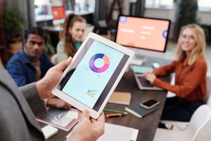 Équipe réunie autour d'une table de travail, une personne montrant un graphique sur une tablette