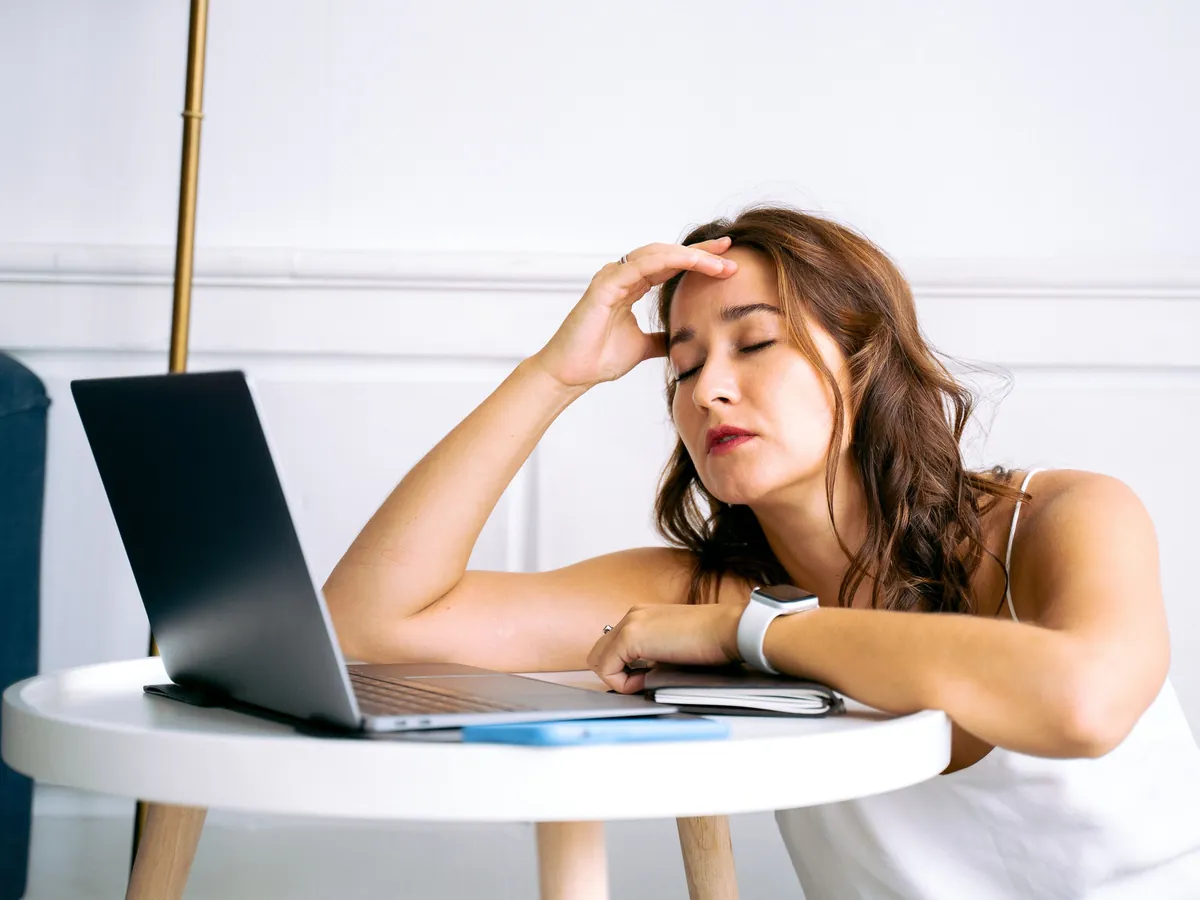 Jeune femme épuisée, la main sur le front, accoudée devant son ordinateur portable
