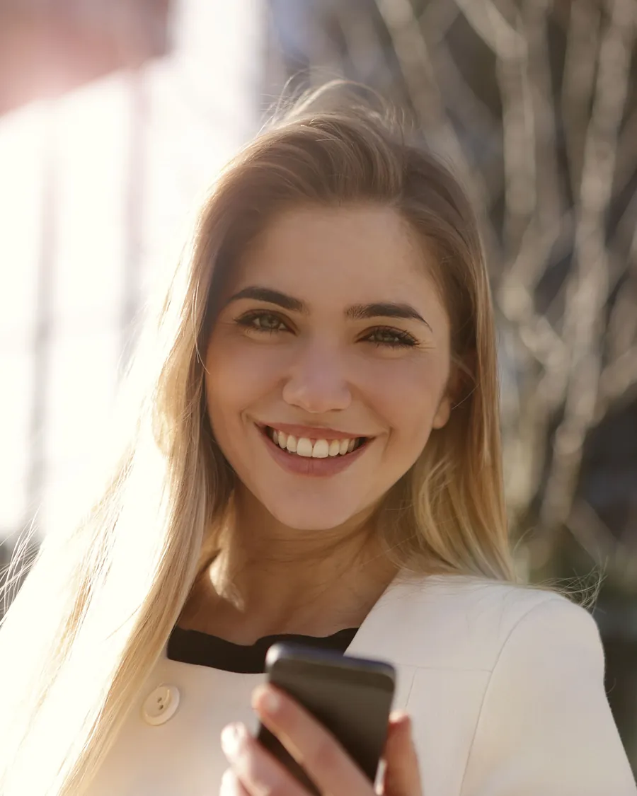 Portrait d'une jeune femme blonde souriante tenant son téléphone, en lumière naturelle
